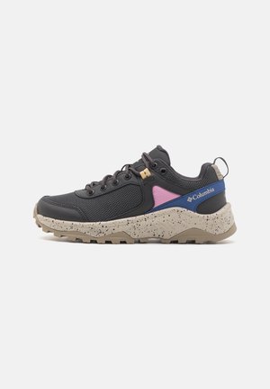 Zapatilla deportiva negra con parte superior de malla, acentos en púrpura y azul, media suela beige moteada y suela resistente con patrones de tracción.