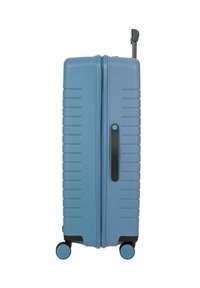 Valigia rigida di colore azzurro chiaro, con una texture a righe, maniglia nera e quattro ruote per la mobilità.