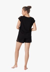 Czarny komplet piżamowy z krótkim rękawem i szortami, ozdobiony koronkowymi detalami na ramionach i bokach. Miękka tkanina i luźny krój.
