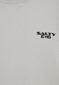 Világosszürke pulóver bordázott nyakkivágással, fekete "SALTY D.G" logóval és texturált varrási részlettel a galléron.