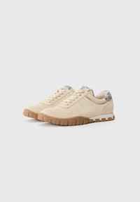 Beige semskede lave sneakers med teksturert gummisåle, med gullsnører og mønstret bakre krage.