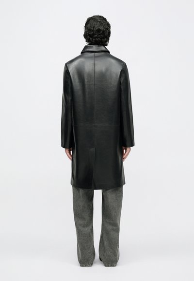 Schwarzer Lederjacke mit geradem Schnitt, Kragen und langen Ärmeln, kombiniert mit grauen, weit geschnittenen Hosen. Glatte Struktur und minimalistisches Design.