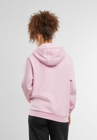 Rožinė pūkinė striukė su ilgomis rankovėmis, minkšta medžiaga, kengūros kišenė ir raštuoti rankogaliai bei apatinė dalis, demonstruojanti laisvą prigludimą ir kasdienį dizainą.