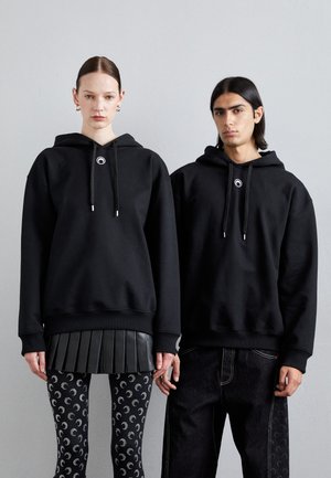 Hanorace negre cu logo pe față, cu șnururi și manșete ribbate. Modelul feminin poartă o fustă plisată; modelul masculin are jeanși din denim închis.