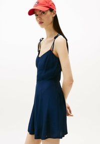 Vestido azul marino con tirantes finos y falda acampanada. Detalles en rojo en los tirantes, malla fina y cierre de cremallera en el lateral.