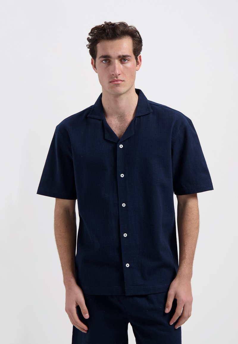 Marineblauw overhemd met korte mouwen van textuurstof, met een opstaande kraag, knoopsluiting en witte knopen.