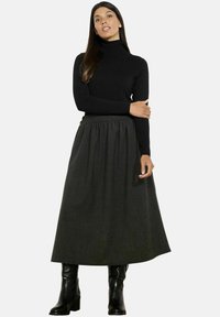 Črna jopica z visokim ovratnikom v kombinaciji z dolgo, temno sivo, teksturirano krilo. Model nosi črne škornje do kolen, ki prikazujejo gladko tkanino in zbrano pasnico.