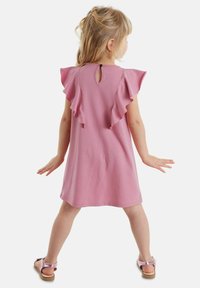 Růžové bavlněné šaty s volánkovými rukávy, detail s klíčovou dírkou na zadní straně a kulatým lemem. Pár světle růžových sandálů s páskem a plochou podrážkou.