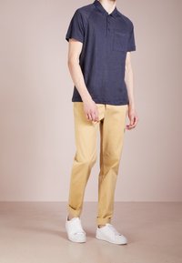 Navy short-sleeve polo with a chest pocket, paired with beige chinos and white sneakers. Casual fit, soft texture, and rolled cuffs.