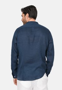 Camicia a maniche lunghe blu navy in lino con orlo curvo, polsini con bottone e colletto classico. Texture liscia con dettagli di design minimi.