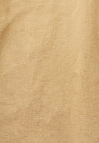 Tissu beige grossier tissé montrant une texture naturelle de lin avec des fils visibles et de légers plis.