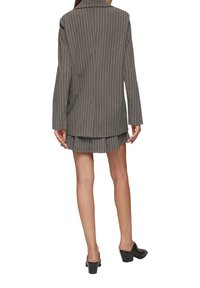 Blazer gris �à rayures fines avec une coupe légèrement oversize, associé à une jupe mini plissée assortie et des mules à talons carrés noirs.