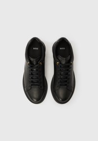 Paar schwarze Leder-Sneaker mit Schnürung, goldenen Ösen und "BOSS"-Markenlogo auf der Zunge und der Innensohle, von oben auf weißem Hintergrund gezeigt.
