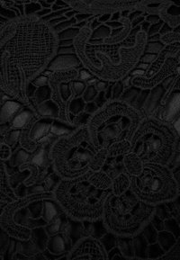 Tessuto in pizzo nero con intricati motivi floreali e geometrici, caratterizzato da una superficie morbida e testurizzata contro uno sfondo liscio.