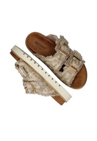 Bežové látkové klouzavé sandály s třepícími se okraji, dvojitými kovovými přezkami, malými zlatými hřebíčky a bílou gumovou podrážkou s texturovaným detailem.