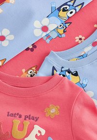 Tre färgglada sweatshirt: rosa med texten "låt oss leka" och blommor, ljusblå med tecknade figurer och blommönster.
