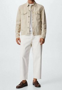 Chaqueta de mezclilla beige con bolsillos de solapa, camisa blanca, pantalones anchos blancos y mocasines marrones. Textura suave, ajuste casual. Diseño minimalista.