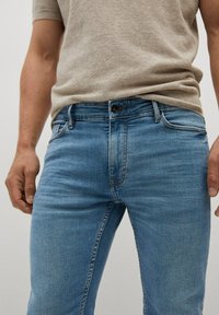 Jeans de denim azul claro con un corte recto, que cuentan con un diseño clásico de cinco bolsillos, ligero desgaste en la tela y un cierre de botón en la cintura.