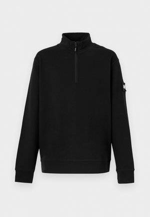 Musta pitkähiha-pulloveri, jossa pystyskaulus, puolivetoketju edessä, resorireunaiset hihansuut ja pieni tasku vasemmassa hihassa.