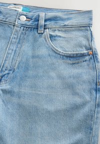 Jeans en denim bleu clair en gros plan montrant la poche avant, la taille avec bouton, les passants de ceinture et l'étiquette « ANKLE STRAIGHT » à l'intérieur de la taille.