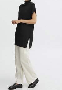 Svart kortärmad topp med hög krage, tillsammans med krämfärgade corduroybyxor med vida ben och svarta klumpiga skor. Sidöppningar i toppen.