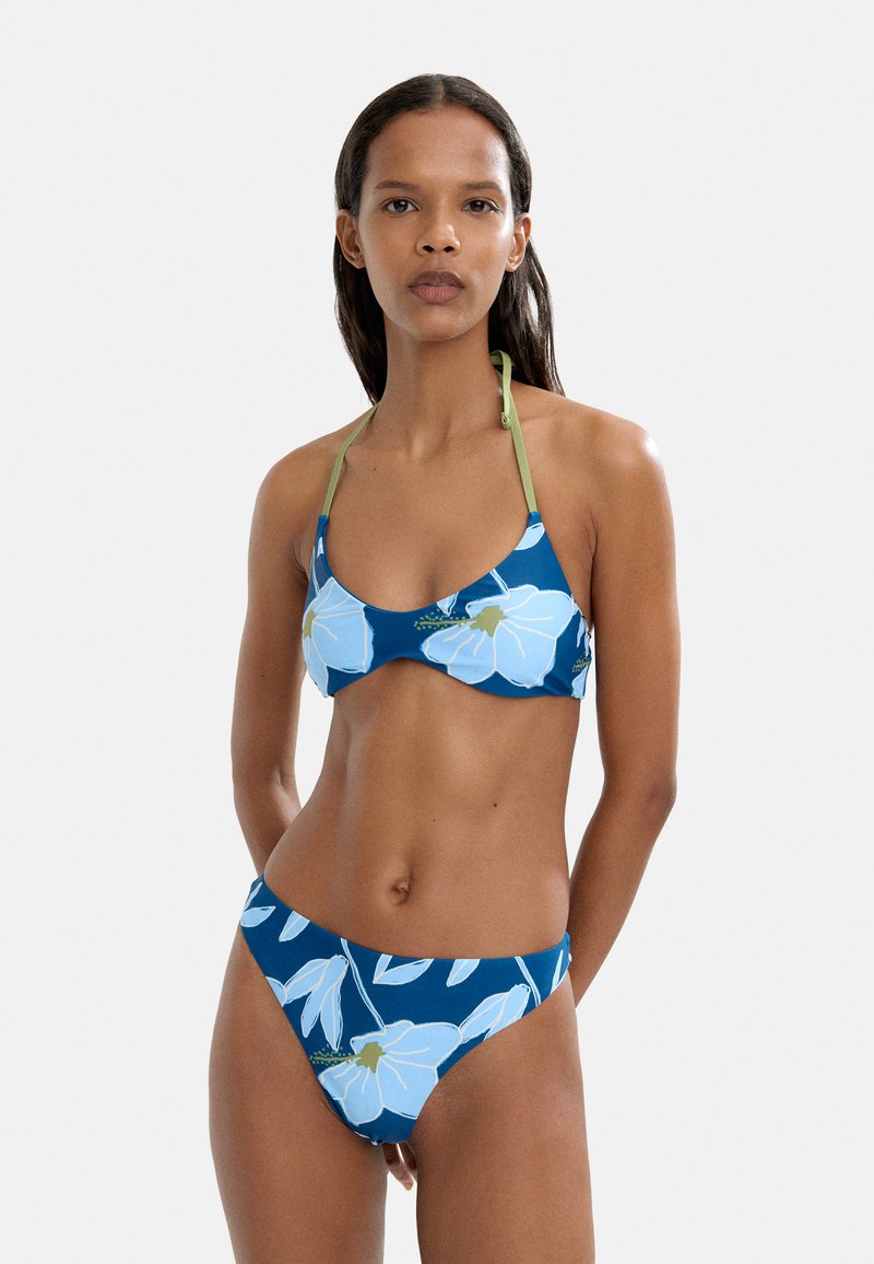 Niebieski zestaw bikini z kwiatowym wzorem w jasnoniebieskie kwiaty. Górna część ma okrągły dekolt i cienkie zielone ramiączka; majtki są w stylu low-rise.