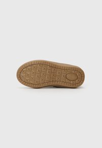 Suela de un zapato con una superficie texturizada, de color marrón claro y un patrón de estrellas y surcos para tracción. Forma plana y redondeada.
