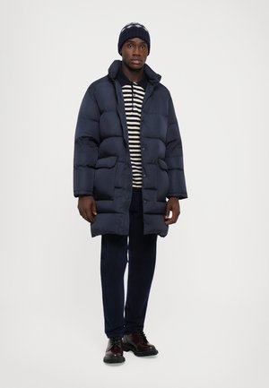 Navy puffer jacket with a high collar, paired with a striped long-sleeve shirt, dark pants, and brown lace-up boots.