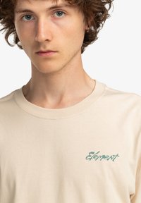 Beige cotton t-shirt with a crew neckline, featuring a green "Element" logo on the left chest area. Smooth texture, simple design.