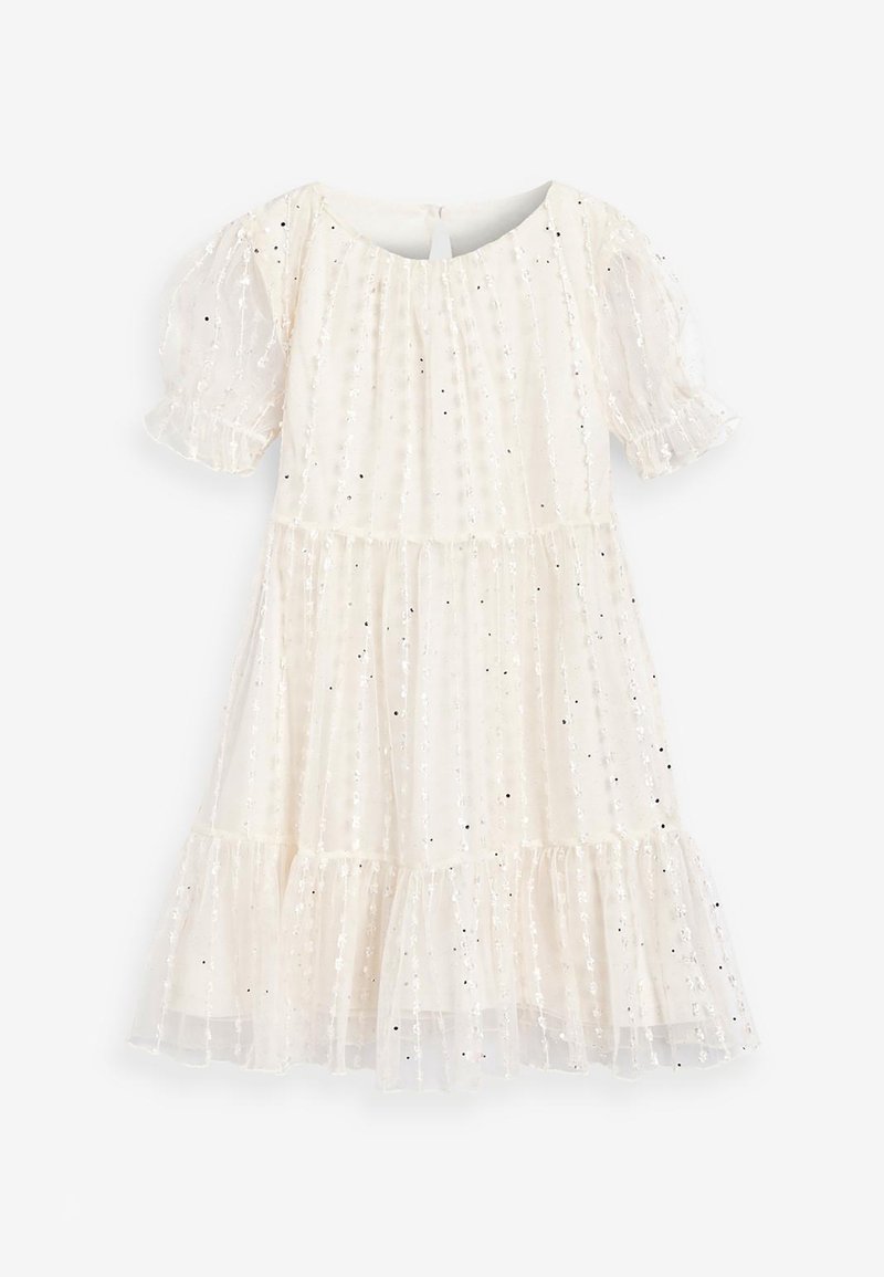 Abito bianco con maniche a sbuffo, volants a strati e decorativi paillettes argentate su un tessuto trasparente. Presenta un colletto rotondo e chiusura sul retro.