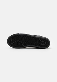 Black rubber sneaker sole with a herringbone pattern, textured surface, and rounded shape; no additional details or markings visible.