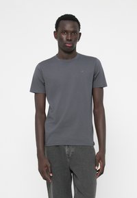 Tricou cu mânecă scurtă și gât rotund, din bumbac gri închis, cu un logo discret pe piept. Asortat cu blugi din denim gri.