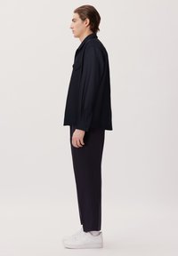 Marineblaues Shirt mit entspannter Passform, langen Ärmeln und einer aufgenähten Tasche, kombiniert mit engen schwarzen Hosen und weißen Turnschuhen.