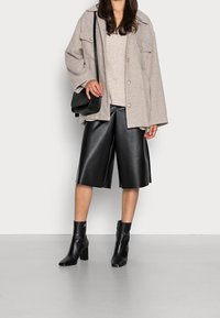 Manteau gris oversized, pull en tricot beige, culottes en cuir noir et bottines noires. Fleurs aux textures et couleurs variées.