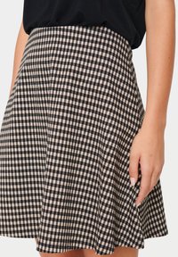 Svart och beige rutig kjol i mjukt tyg, med utsvängd design och A-linjeform, med en mjuk textur.