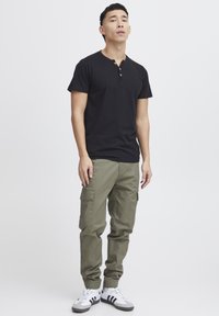 Melnas kokvilnas henley t-krekls ar trim pogām, apvienots ar olīvzaļa krāsas kravas biksēm, kurām ir sānu kabatas un sašaurināti piedurknes. Balti sporta apavi kombināciju noslēdz.