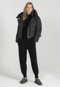 Czarna kurtka puchowa z kapturem, z zamkiem z przodu i pikowanym wzorem. Nosi się ją na czarnym swetrze, w zestawieniu z czarnymi spodniami i loafersami.