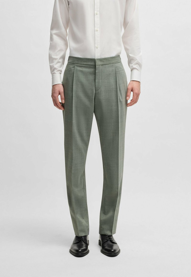 Light green tailored trousers with a textured fabric, wide pleats, and a smooth waistband, paired with black dress shoes and a white shirt.
