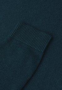 Tessuto lavorato a maglia color teal con dettagli di polsini a coste, che mostra una texture liscia e un motivo uniforme su tutta la superficie.