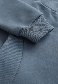 Weiches blaues Sweatshirt mit gerippten Bündchen und glatter Textur. Der Stoff zeigt leichte Farb- und Oberflächenvariationen.