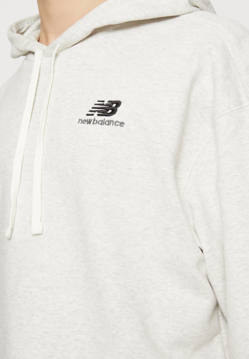 Hoodie gris clair en tissu doux. Comprend une poche kangourou, une capuche avec cordon de serrage réglable et un petit logo noir brodé sur la poitrine.