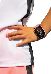 Smartwatch con un cinturino in tessuto rosa, che mostra l'ora in un formato digitale colorato. Una mano poggia su una maglietta atletica rosa chiaro e nera.