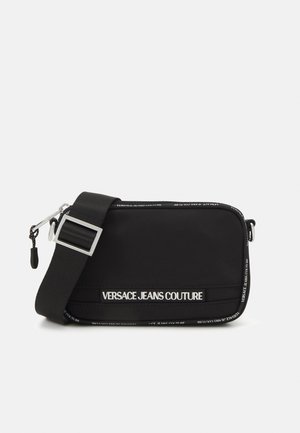 Musta suorakulmainen Versace Jeans Couture -laukku leveällä säädettävällä hihnalla ja logolla, joka on painettu etuosaan ja reunoihin.