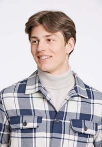 Camicia di flanella a quadri navy e bianchi, con tasche con bottone, colletto e un morbido dolcevita beige sotto.