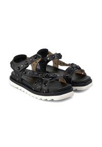 Sandalias negras de cuero, con acentos de tachuelas, correas ajustables y una gruesa suela de goma blanca para mayor tracción.