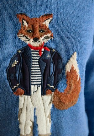 Fox character wearing a navy jacket, red scarf, striped shirt, and white pants embroidered on a blue knitted fabric.