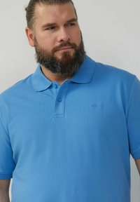 Himmelblaues Poloshirt aus strukturiertem Material, klassischer Kragen, zwei Druckknöpfe und kleines Logo-Detail auf der Brust.