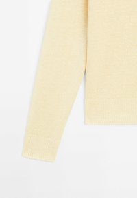 Maglione lavorato a maglia giallo chiaro con un motivo testurizzato, dotato di maniche lunghe e polsini e orli a coste. Finitura in tessuto morbido.