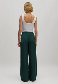 Witte mouwloze top met een lage rug, gecombineerd met losse, groene wijde broek met een elastische tailleband en een gladde textuur.