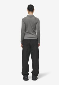 Prigludusi pilka ilgomis rankovėmis palaidinė, juodos krovinių kelnės ir juodi sportbačiai. Palaidinė turi krūtinę ir lygią tekstūrą; kelnės pasižymi kišenėmis ir laisvu siluetu.